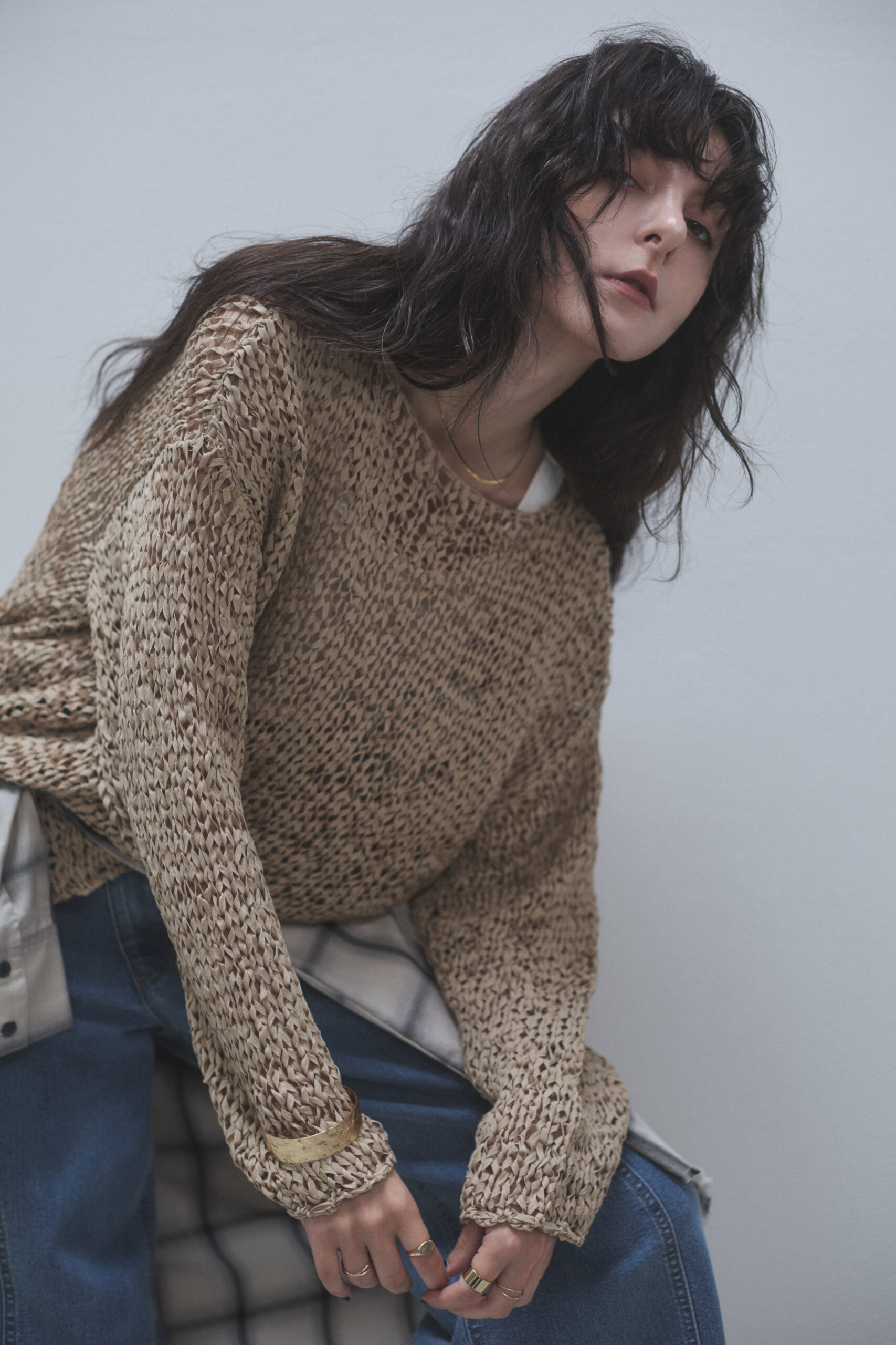 太ケーブル編みセーターとデニムパンツを着てネルシャツを腰に巻いている女性モデル写真