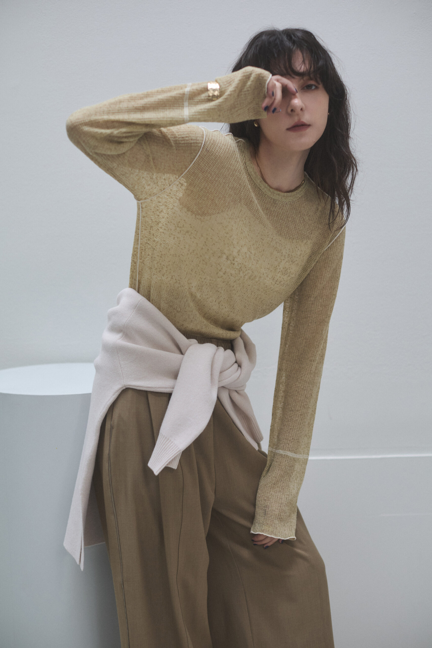 透けているニットプルオーバーとゆるめのストレートパンツを着てセーターを腰に巻いている女性モデルの写真