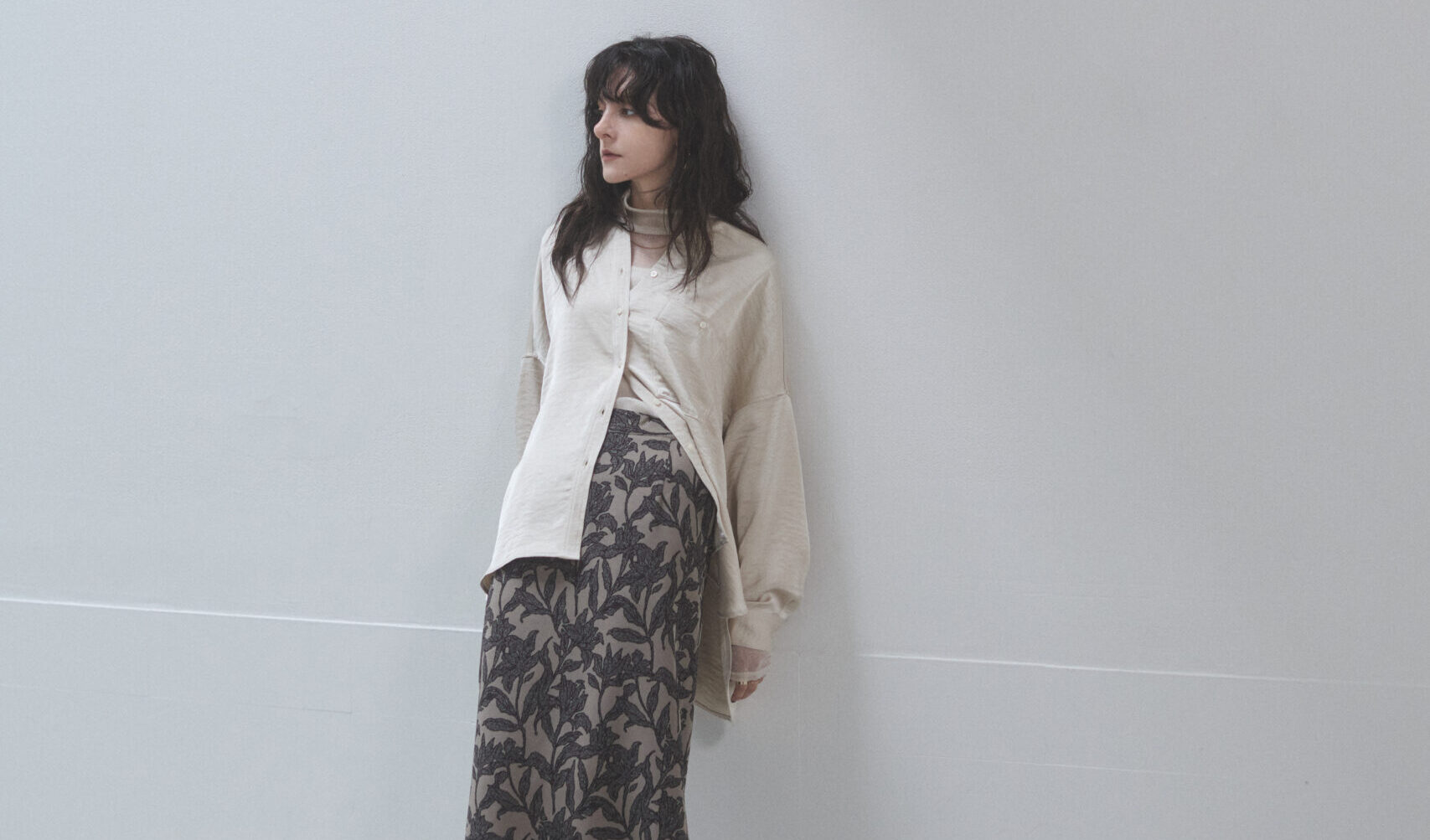 ベージュのサテンシャツと花柄スカートを着ている女性モデルの写真