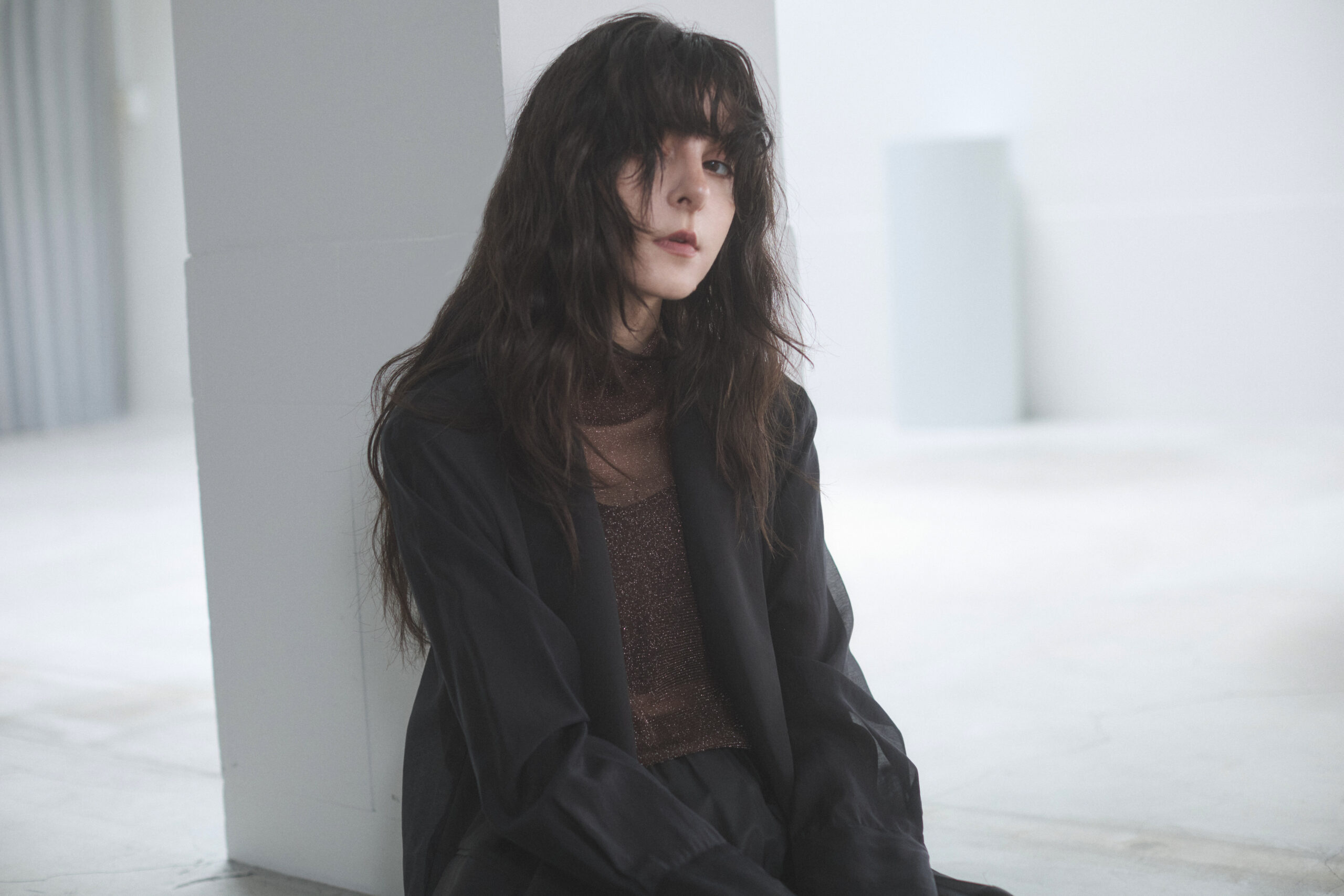 チャコールのジャケットとパンツのセットアップに茶系のインナーを着た女性モデル写真