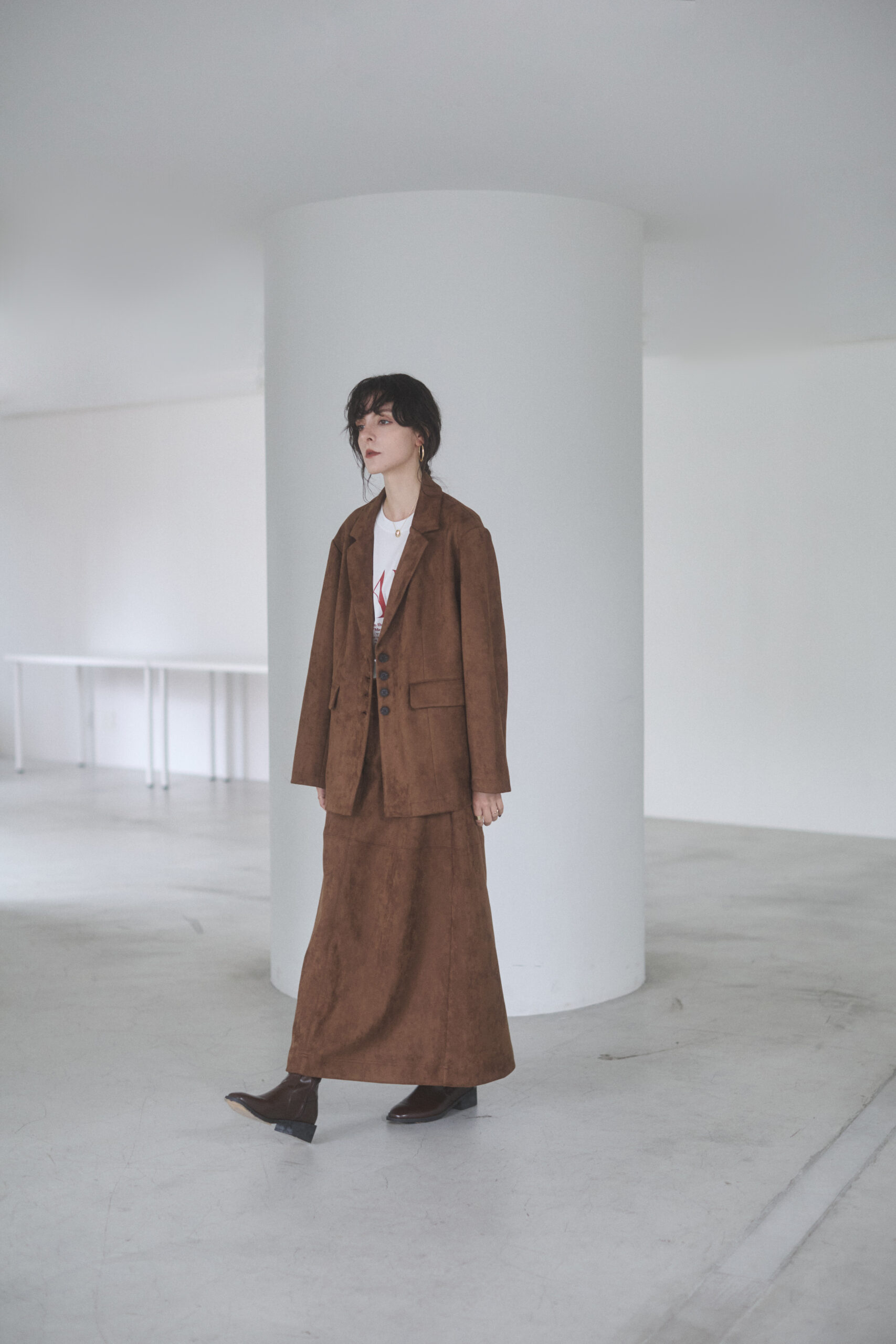 茶色のジャケットとロングスカートのセットアップを着て立っている女性モデル写真