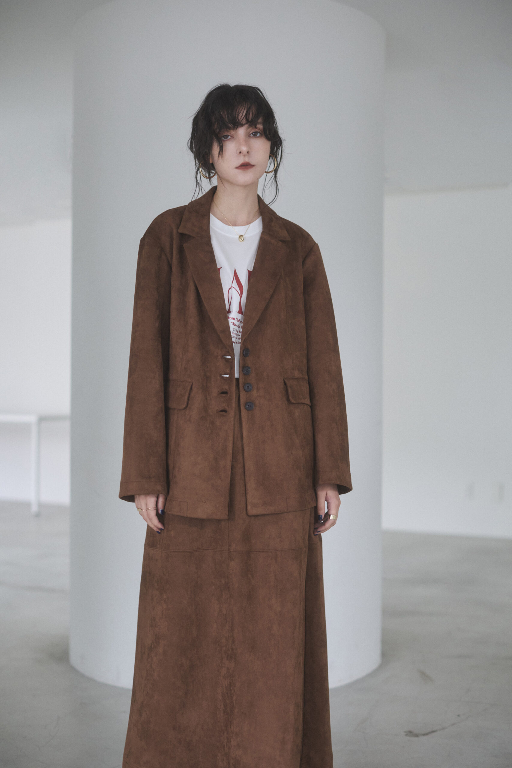茶色のジャケットとロングスカートのセットアップを着て立っている女性モデル写真