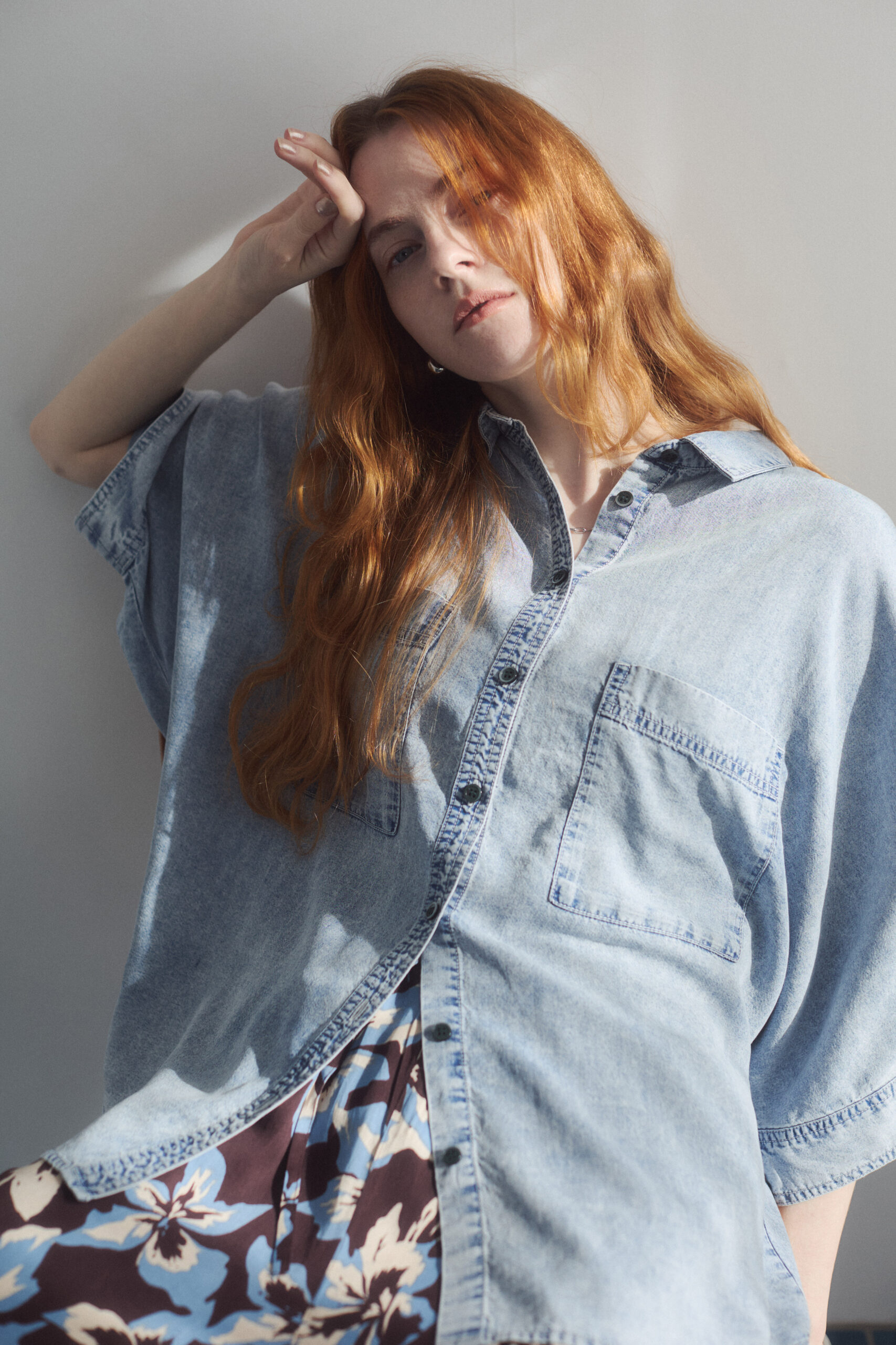 ブリーチデニムシャツと花柄プリントパンツを着て座っている女性モデルの上半身写真