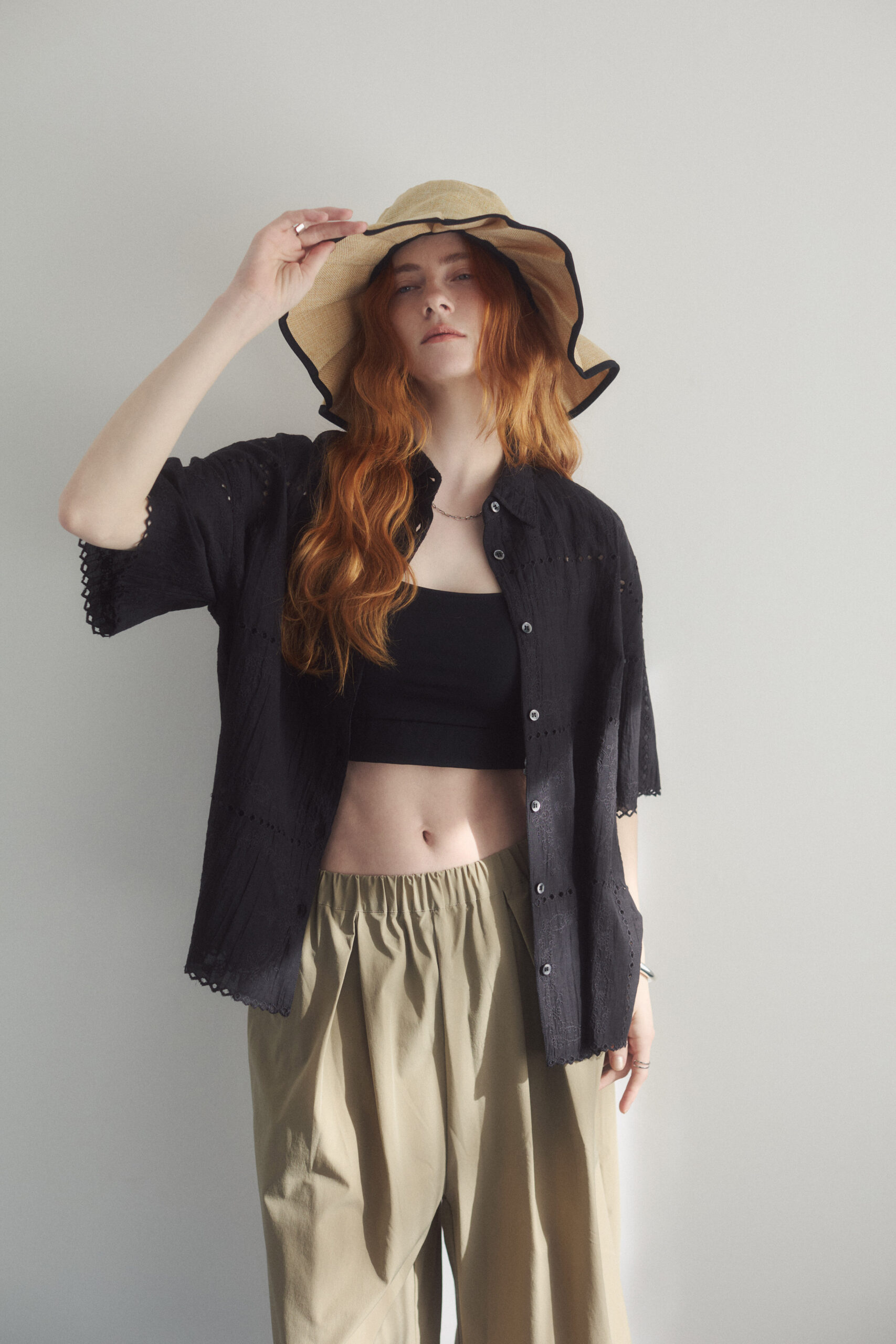 黒いレース半袖ブラウスにタンクトップとベージュのパンツを着て麦わら帽子をかぶっている女性モデル写真