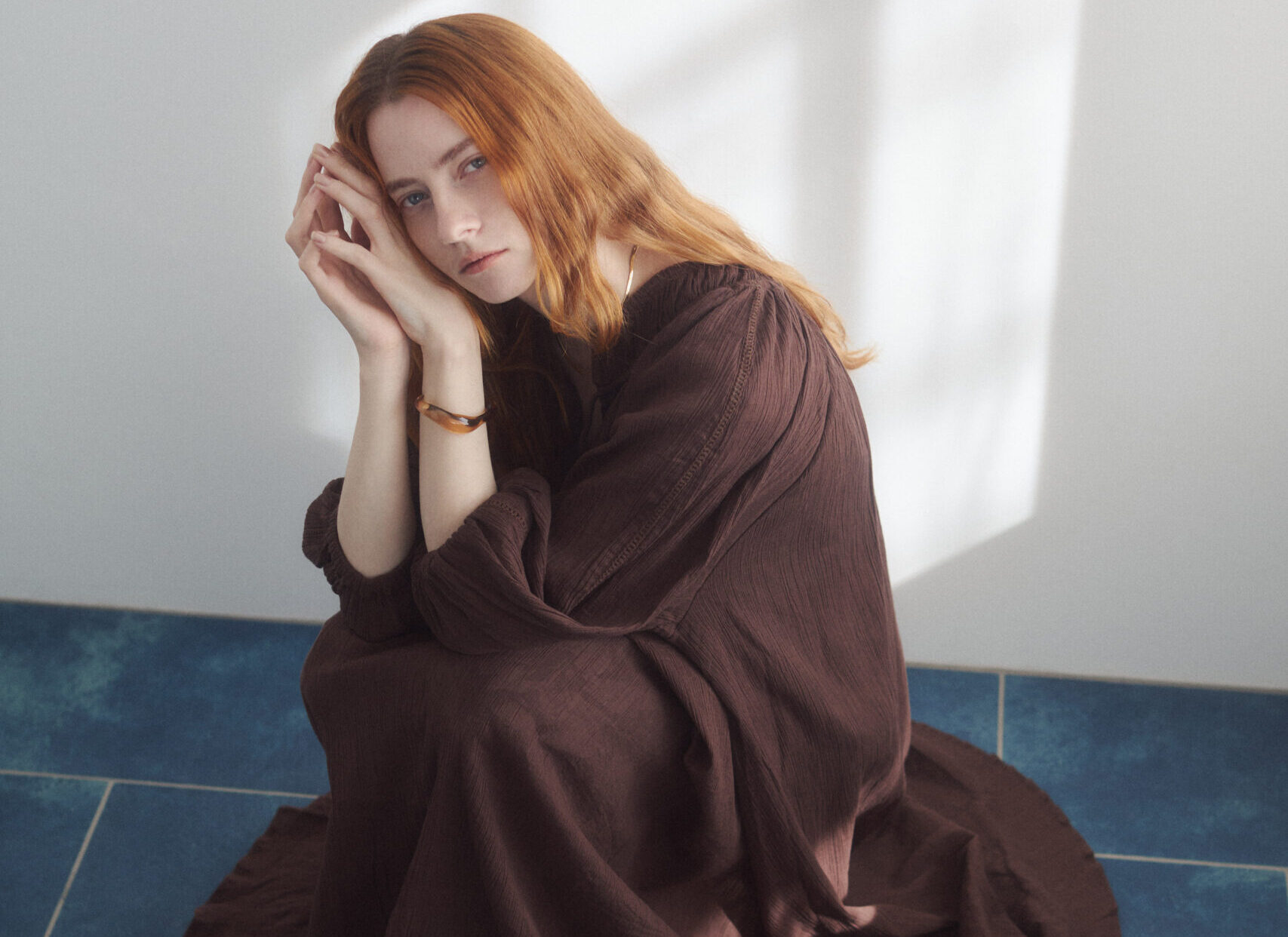 茶色のワンピースを着てしゃがんでいる女性モデルの写真