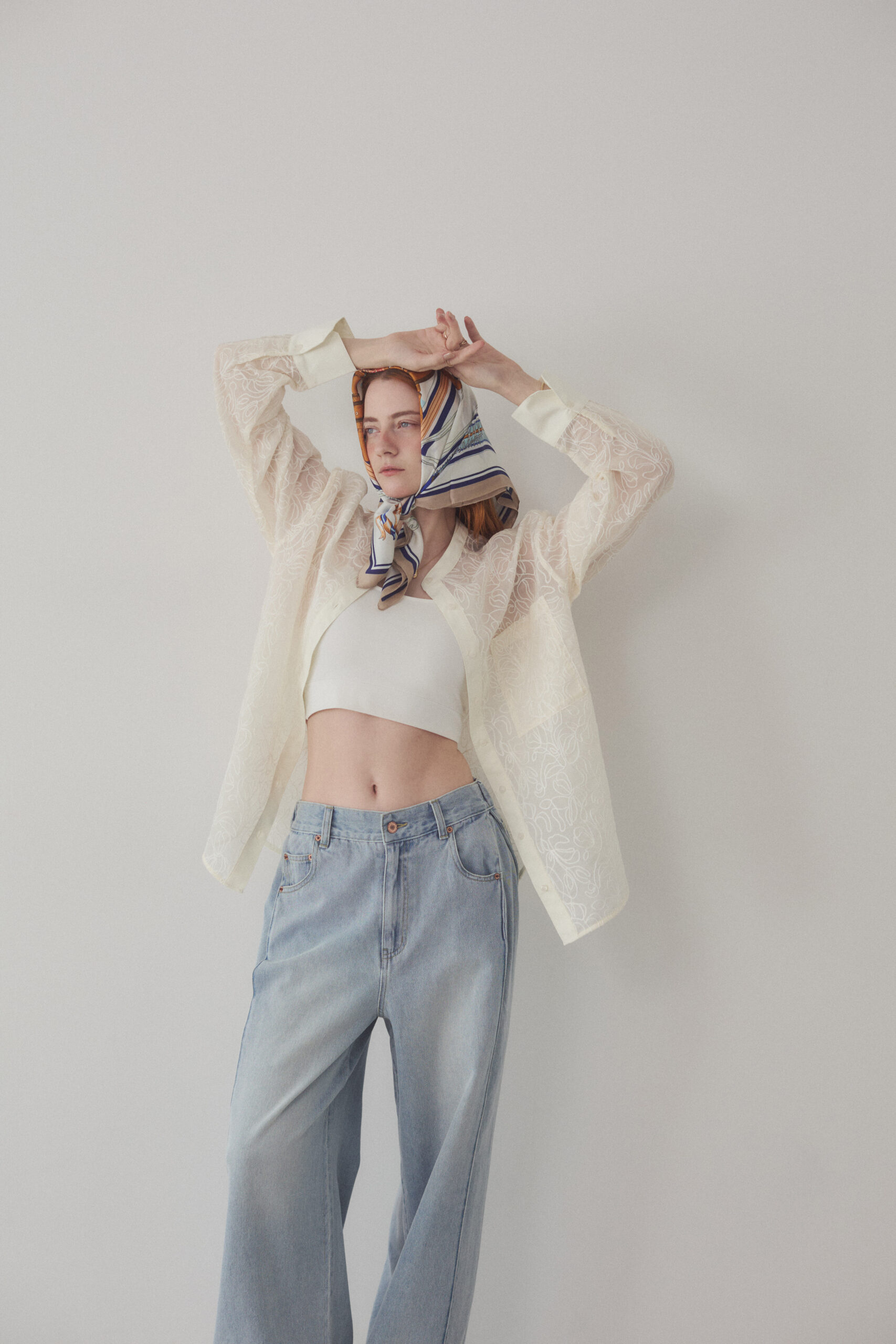 タンクトップとデニムパンツにシアーブラウスを羽織って頭にスカーフを巻いている女性モデル写真