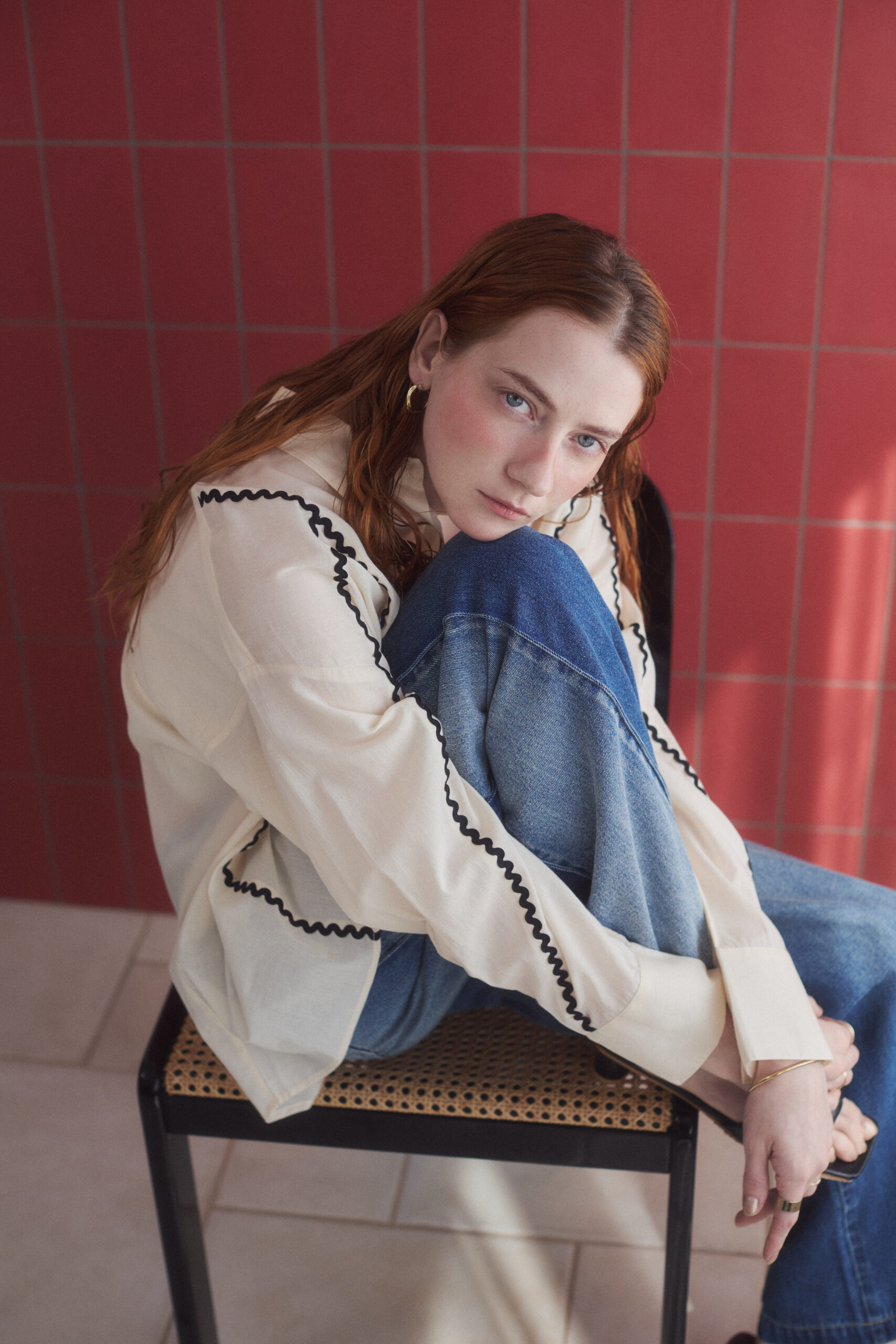 生成りブラウスとデニムパンツを着て椅子に座っている女性モデル写真