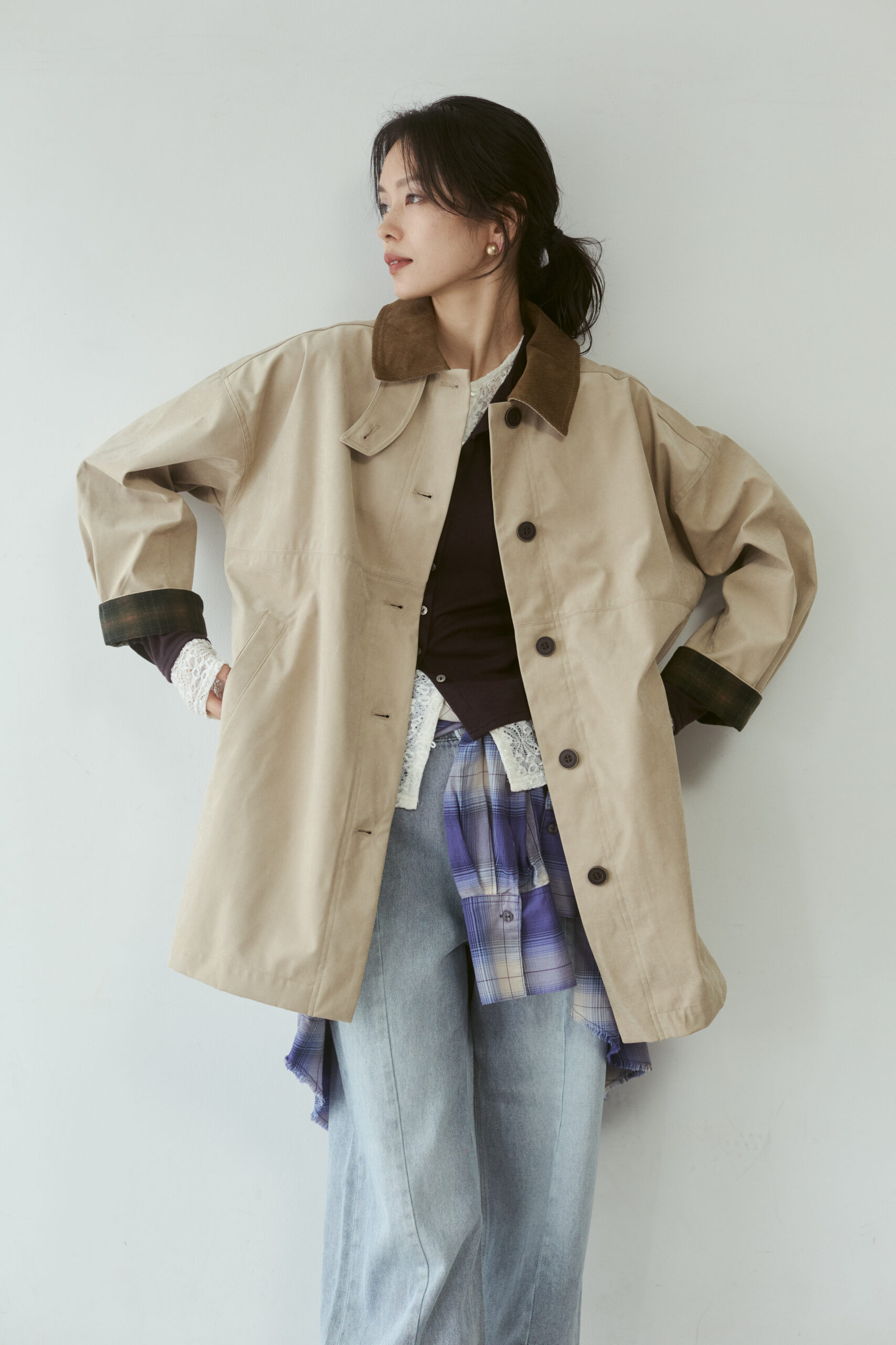 襟は茶色い配色のベージュのコートの中にいろんな服を重ね着している女性モデル写真